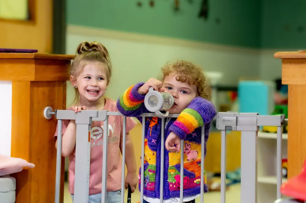 Two toddlers smiling over the classroom gate