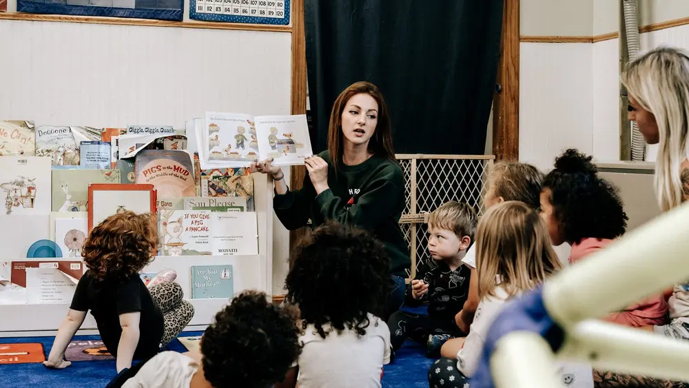 A Kids & Co. teacher reading a picture book to a circle of children